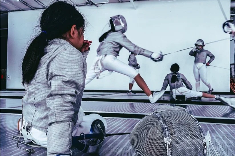 A young fencer watching a match indoors