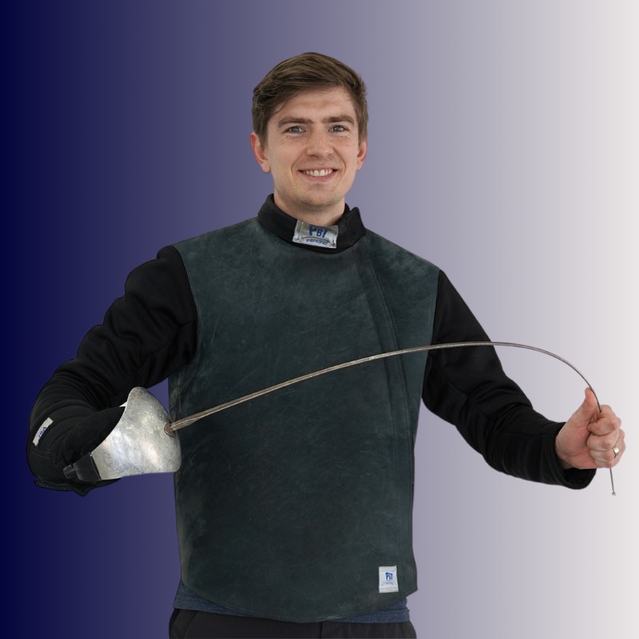 Young man dressed in fencing gear holding a fencing foil and smiling.