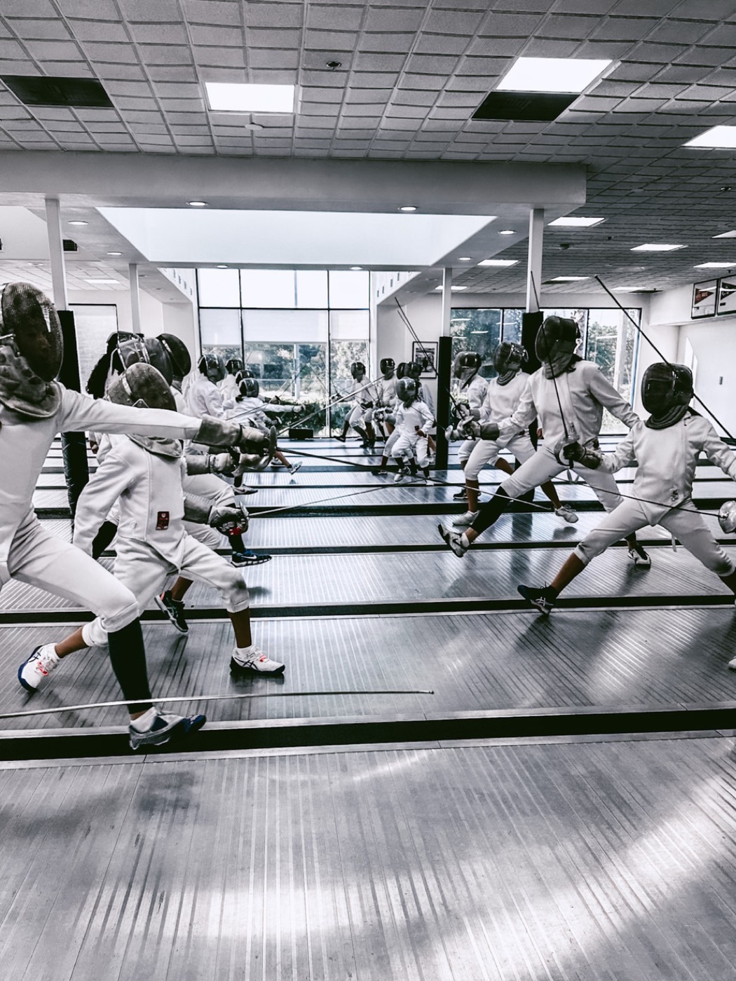 A group practicing fencing in a spacious, well-lit indoor gym